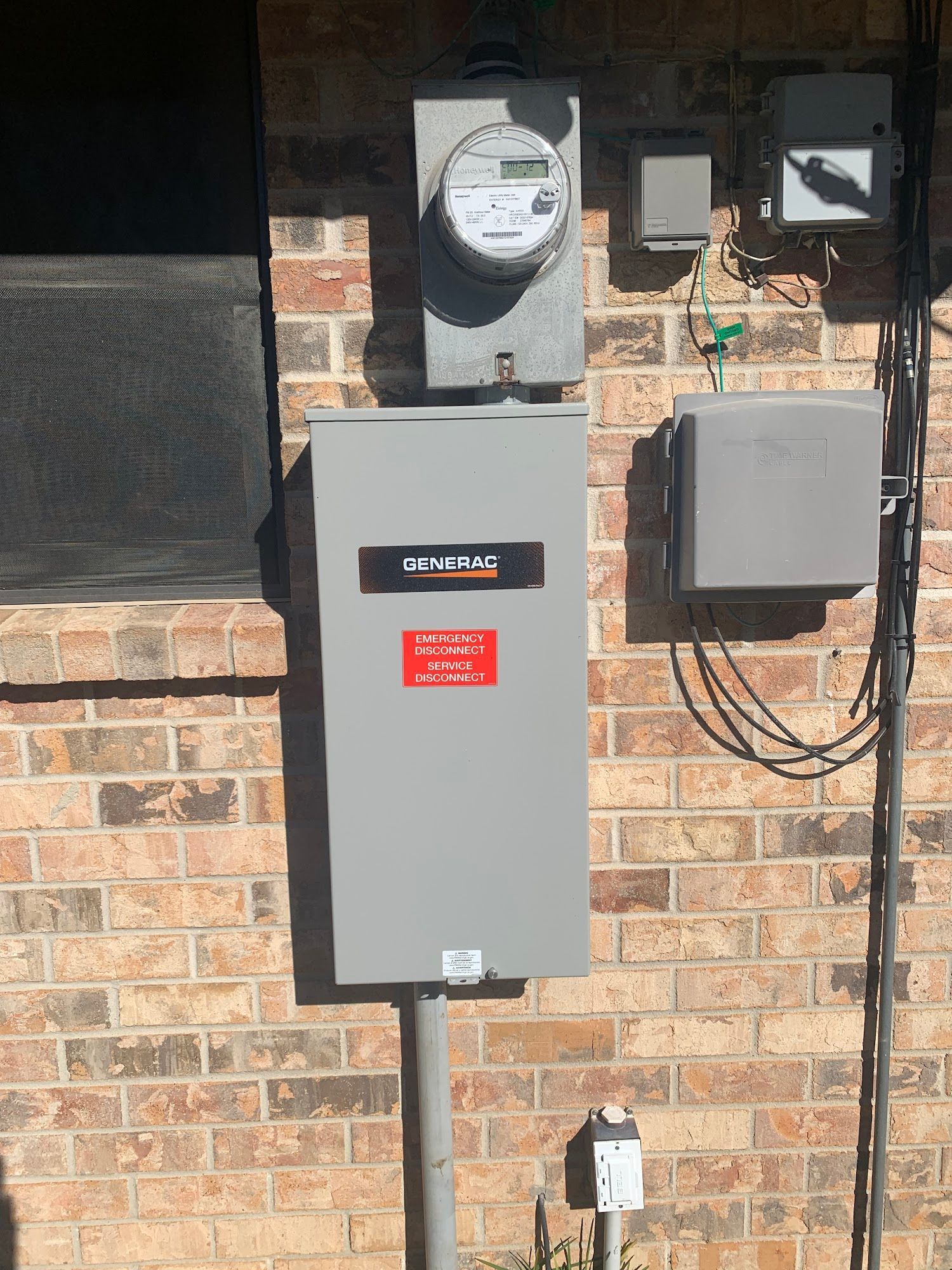 A gray box with a meter on it is attached to a brick wall.