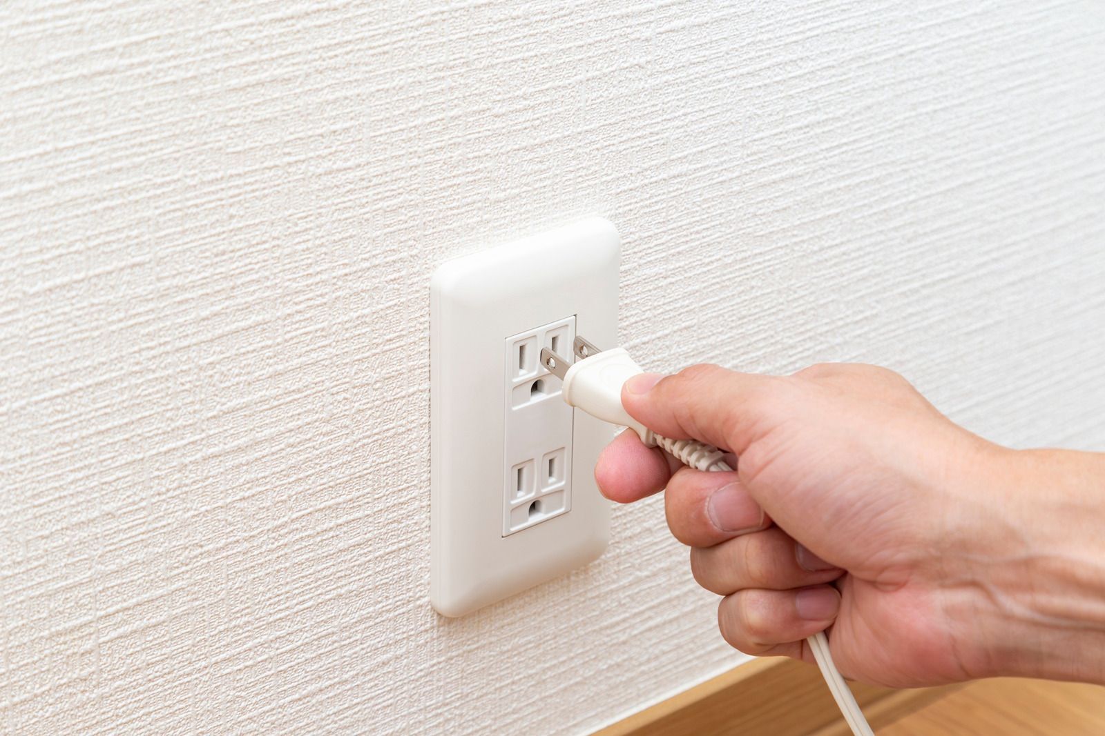 Hand plugging a white cord into a wall outlet.
