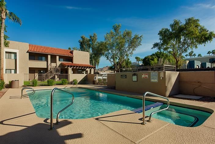 Apartment pool with hot tub, beige deck, and palm trees under a clear blue sky