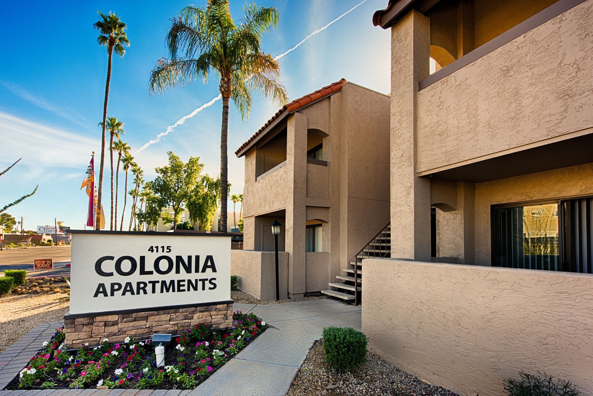 Colonia Apartments sign outside tan apartment buildings with palm trees and desert landscaping.