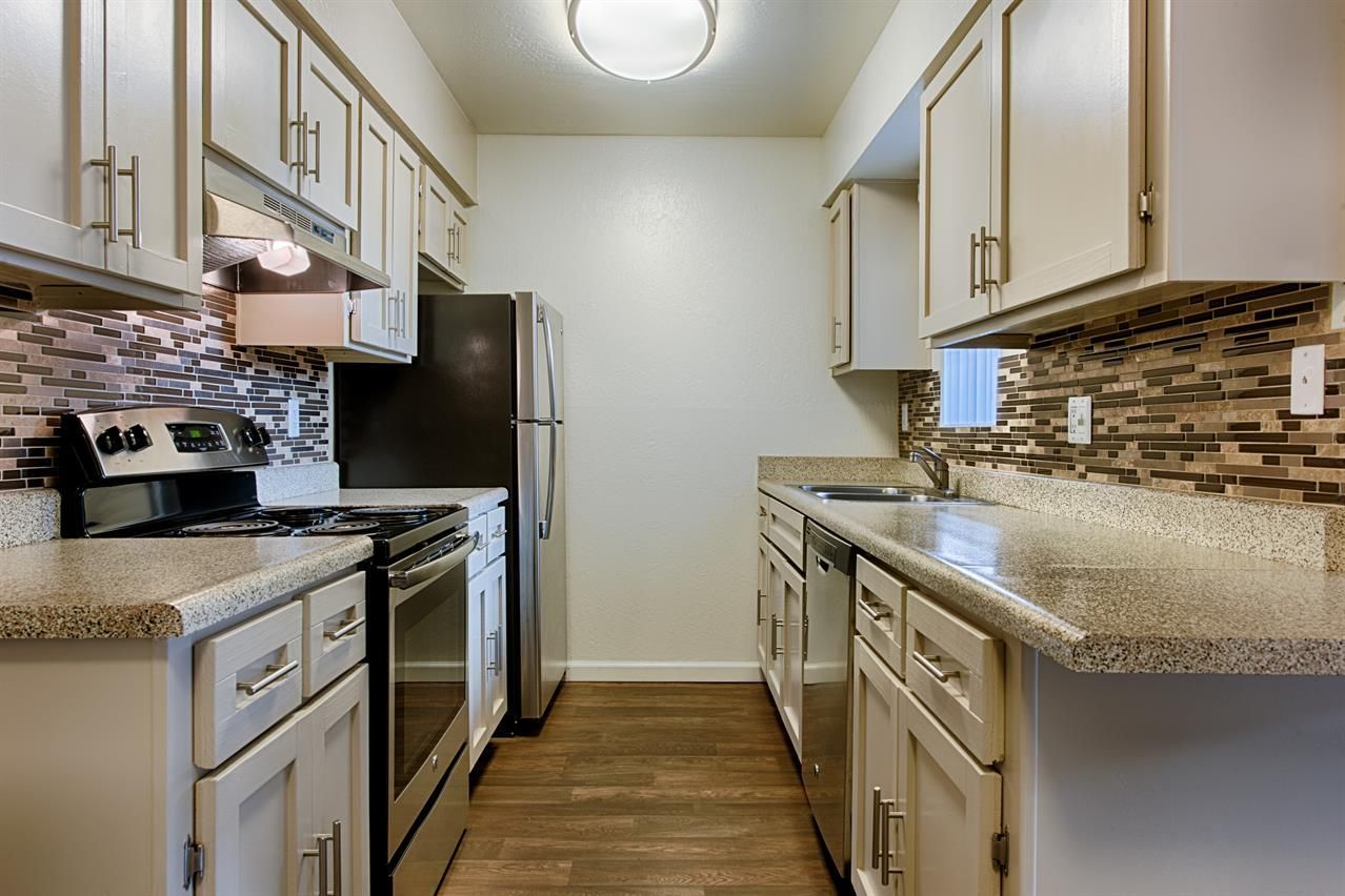 Narrow galley kitchen with white cabinets, granite counters, stainless appliances, and wood-look flooring