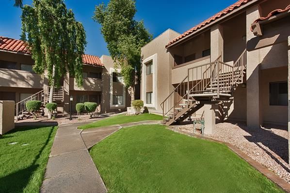 Apartment courtyard with green lawn, trees, and beige buildings with exterior stairs and balconies