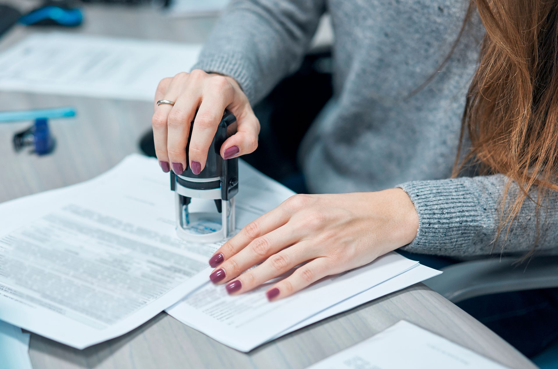 Hands stamping documents on a desk with papers and a pen