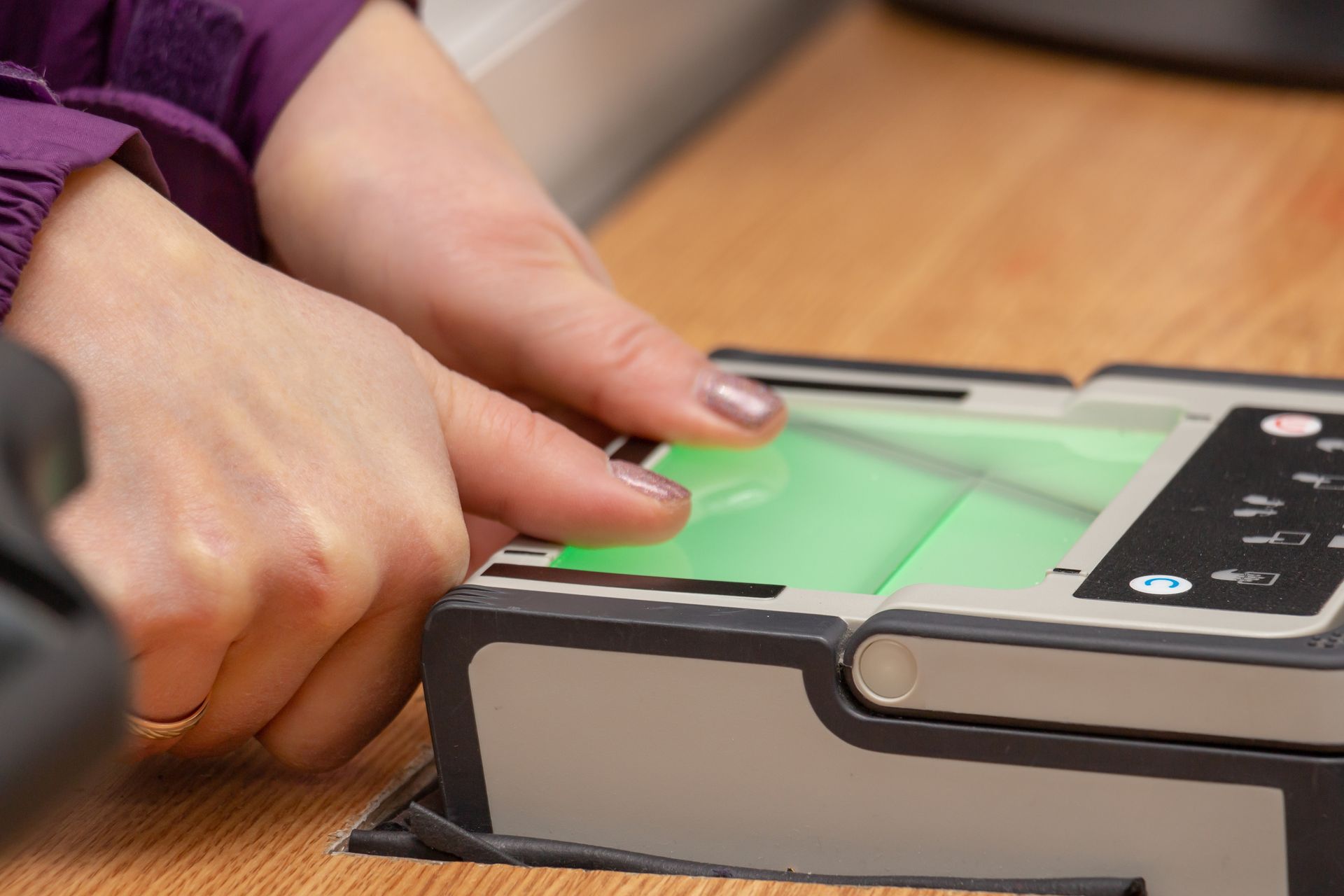 Hands pressing a green fingerprint scanner on a biometric device