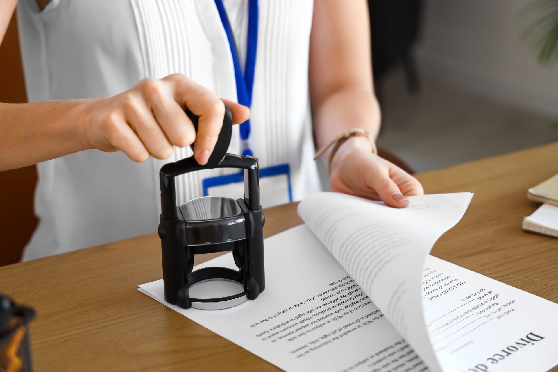 Hands stamping documents at a wooden desk, with a page being flipped over.
