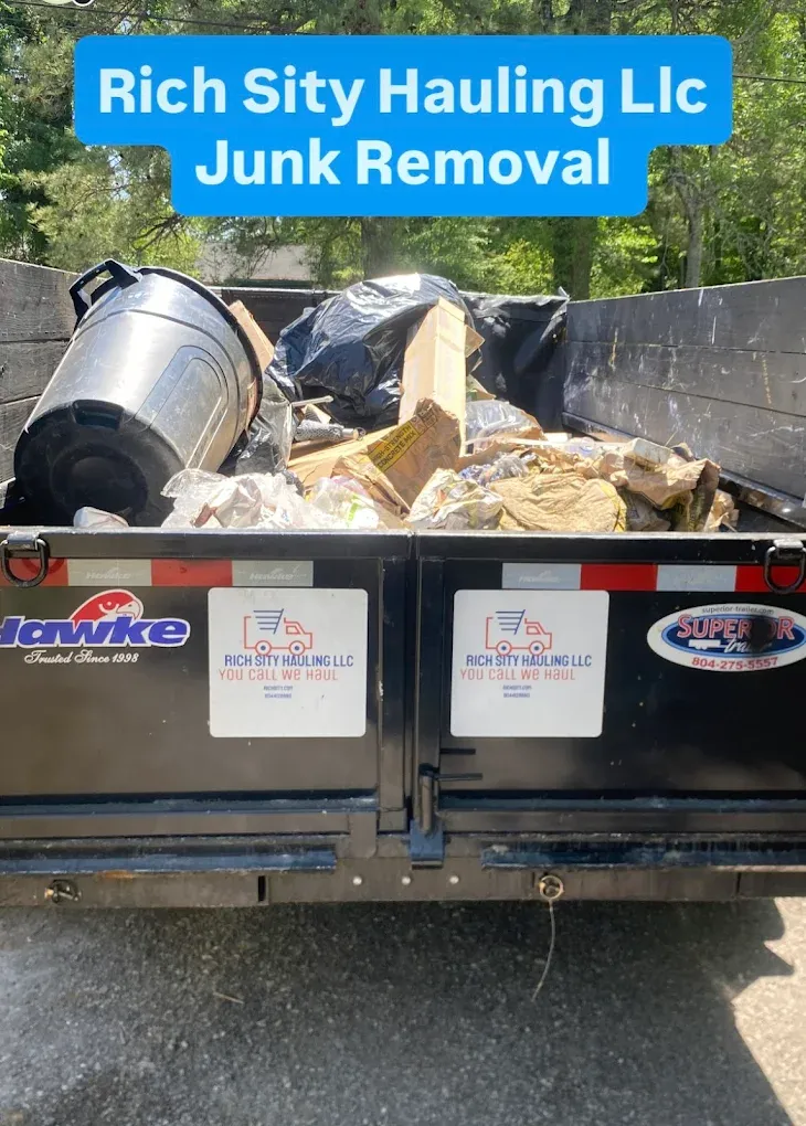 Junk-filled dumpster with trash bags and a fallen metal bin, labeled “Rich City Hauling LLC Junk Removal”