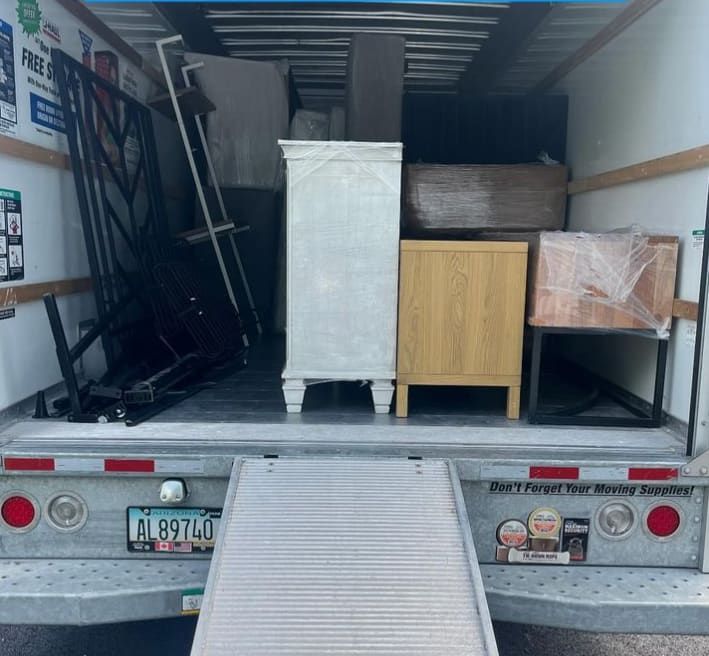 Moving truck loaded with furniture and a metal ladder, viewed from the open rear ramp.