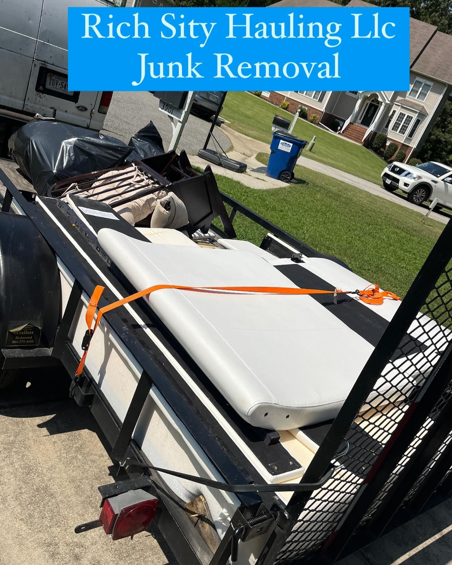 Trailer loaded with junk removal debris, secured by orange straps, with “Rich City Hauling LLC” sign overhead