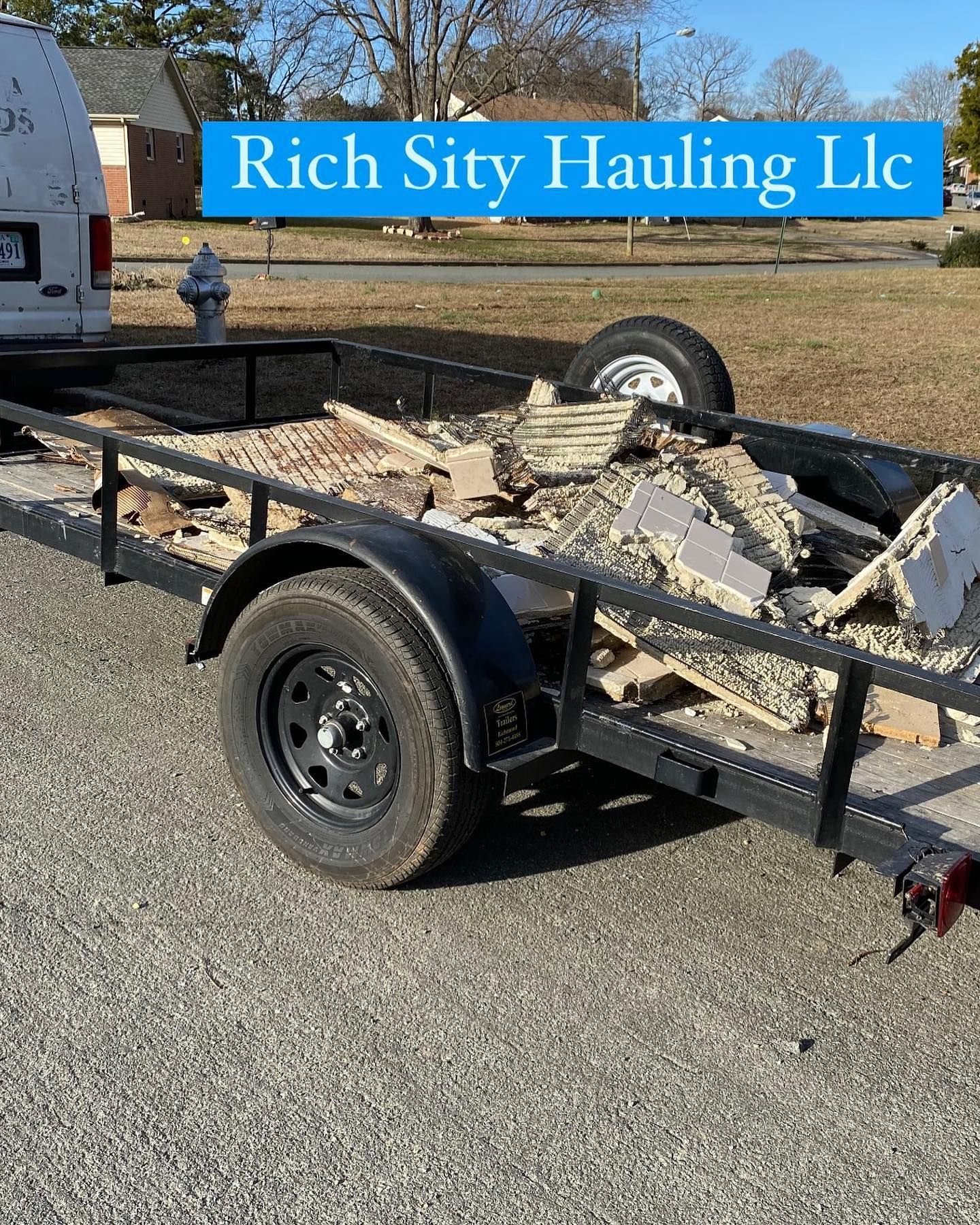 Trailer loaded with broken concrete and debris, parked outdoors in front of a Rich City Hauling sign.