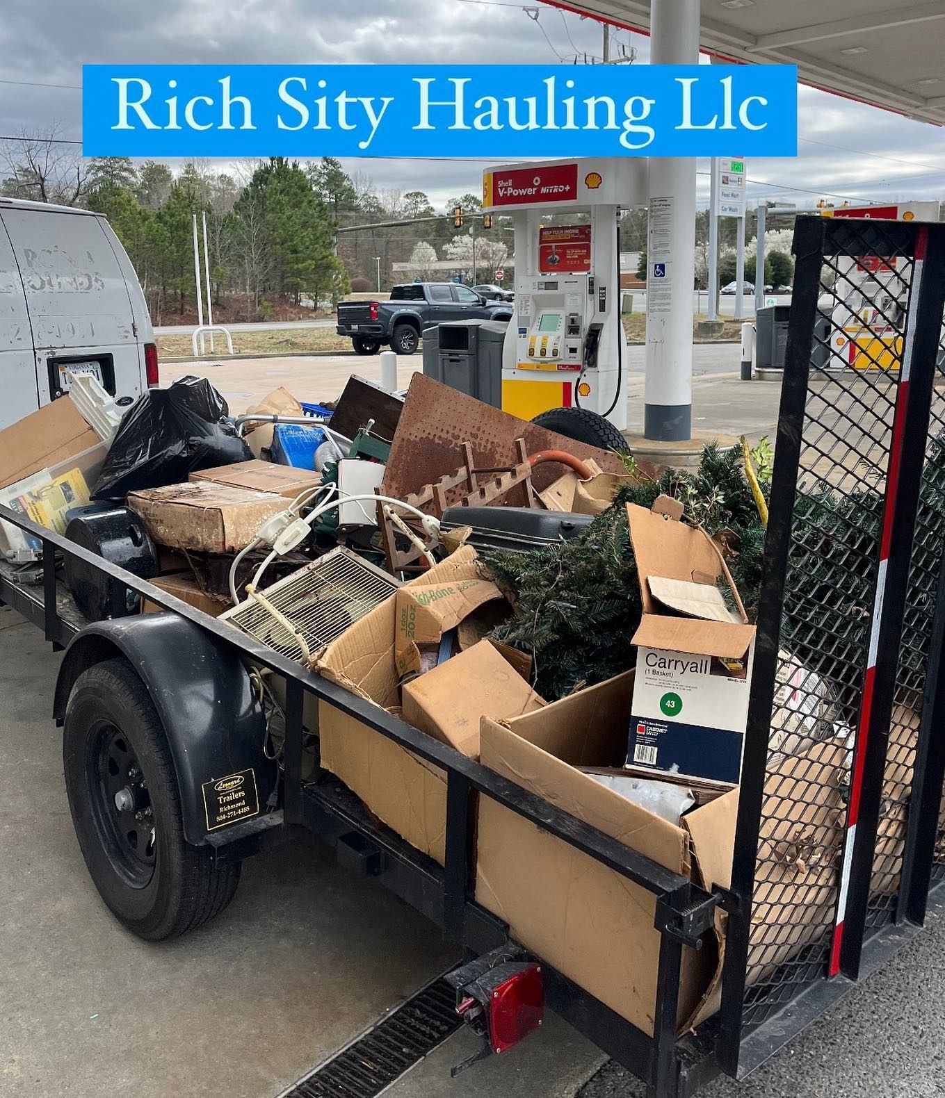 Trash-filled utility trailer at a gas station, with a Rich City Hauling LLC sign overhead.