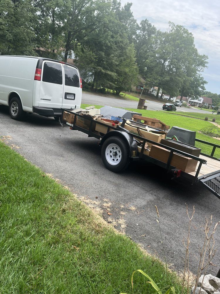 White van parked beside a flatbed trailer loaded with materials on a wet suburban street