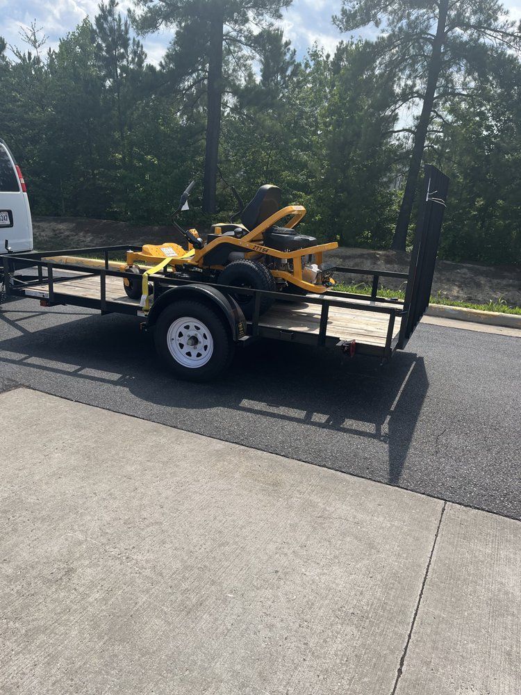 Yellow mower on a black trailer parked by a road in a sunny outdoor lot