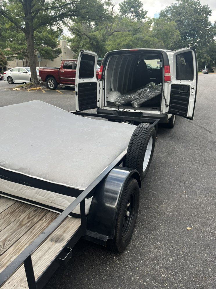 Trailer carrying a white panel beside an open van on a street with parked cars.