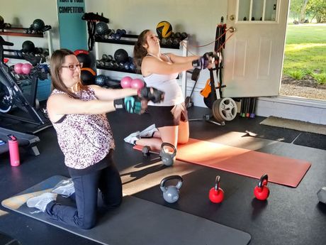 Two women are doing exercises in a gym with dumbbells.