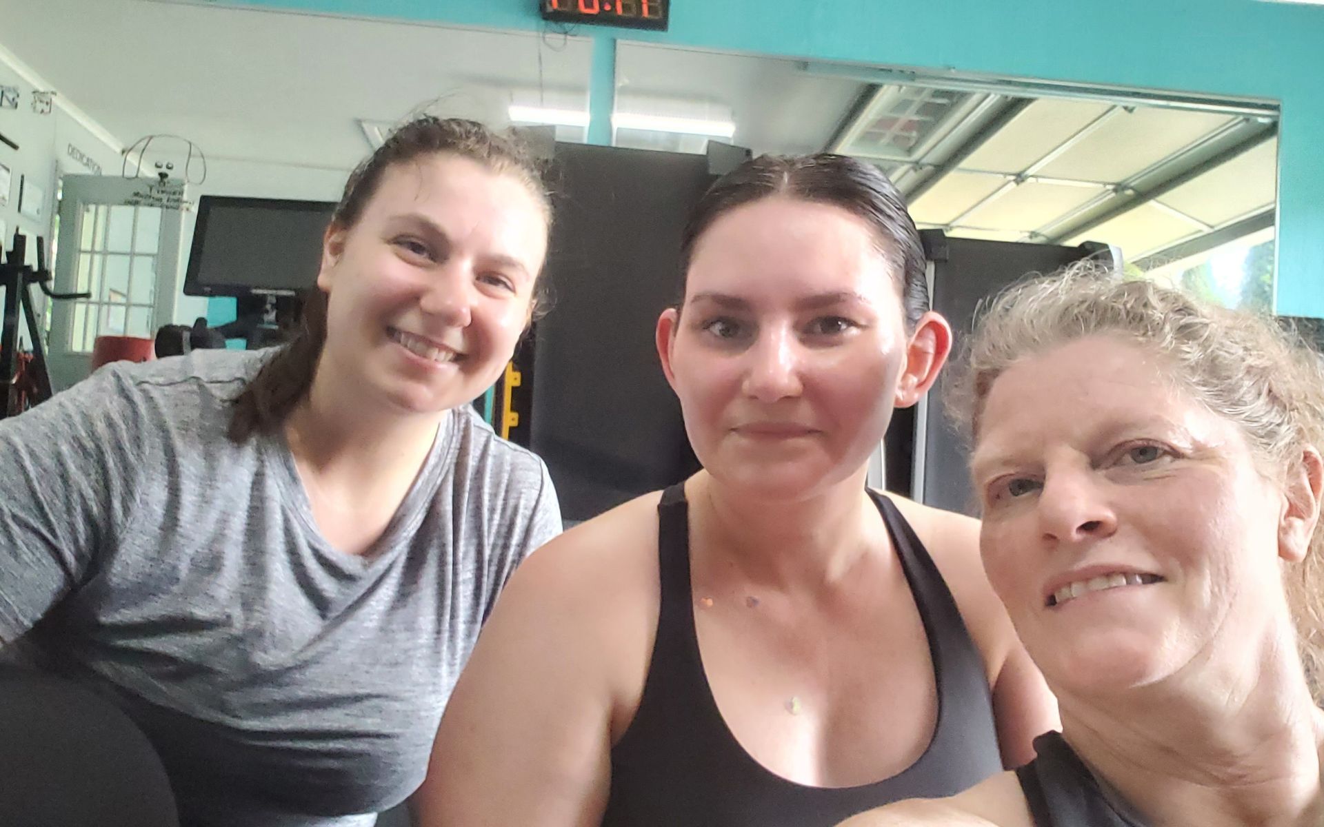 Three people smiling in a gym, two in athletic wear.