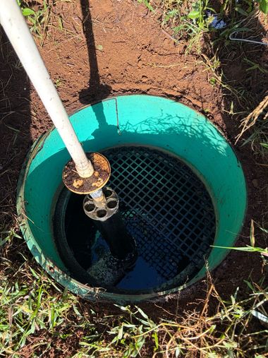 Open green utility well with black mesh cover and a white pipe beside it