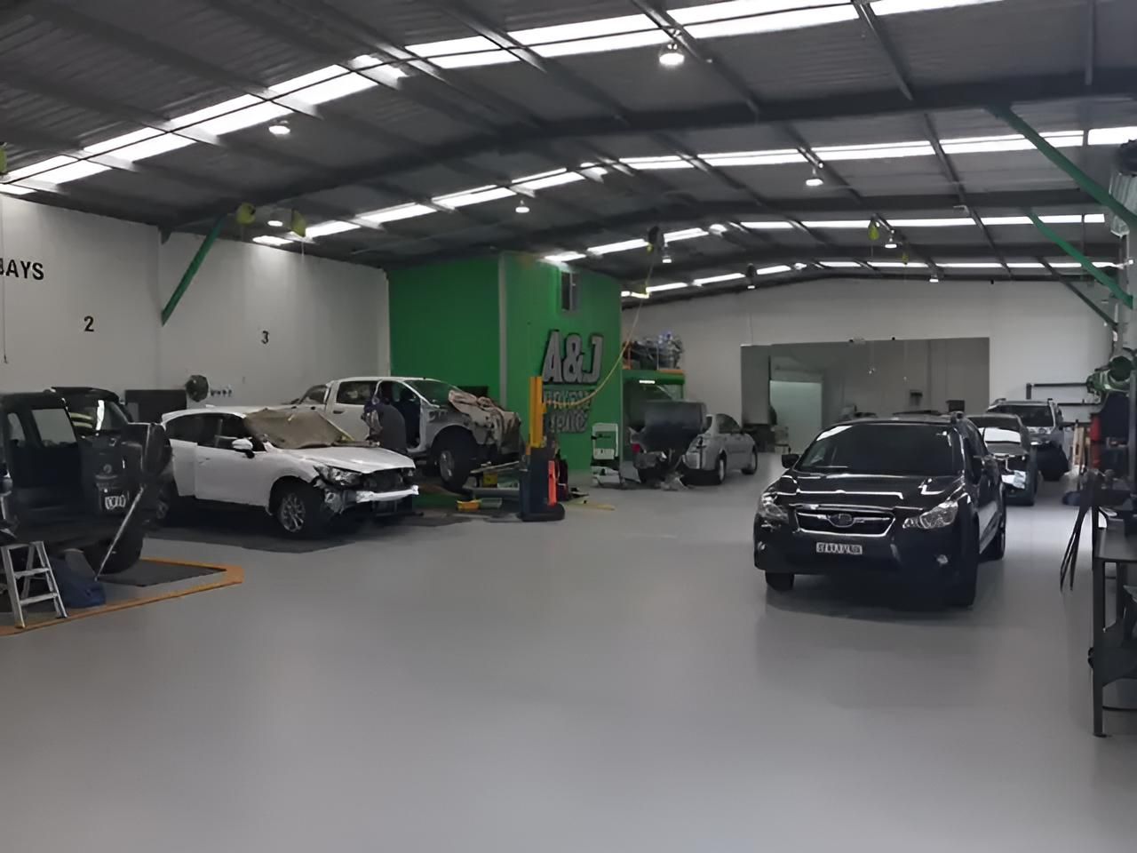A Garage With a Lot of Cars in It and a Green Wall — A & J Auto Body Repairs In Salamander Bay, NSW