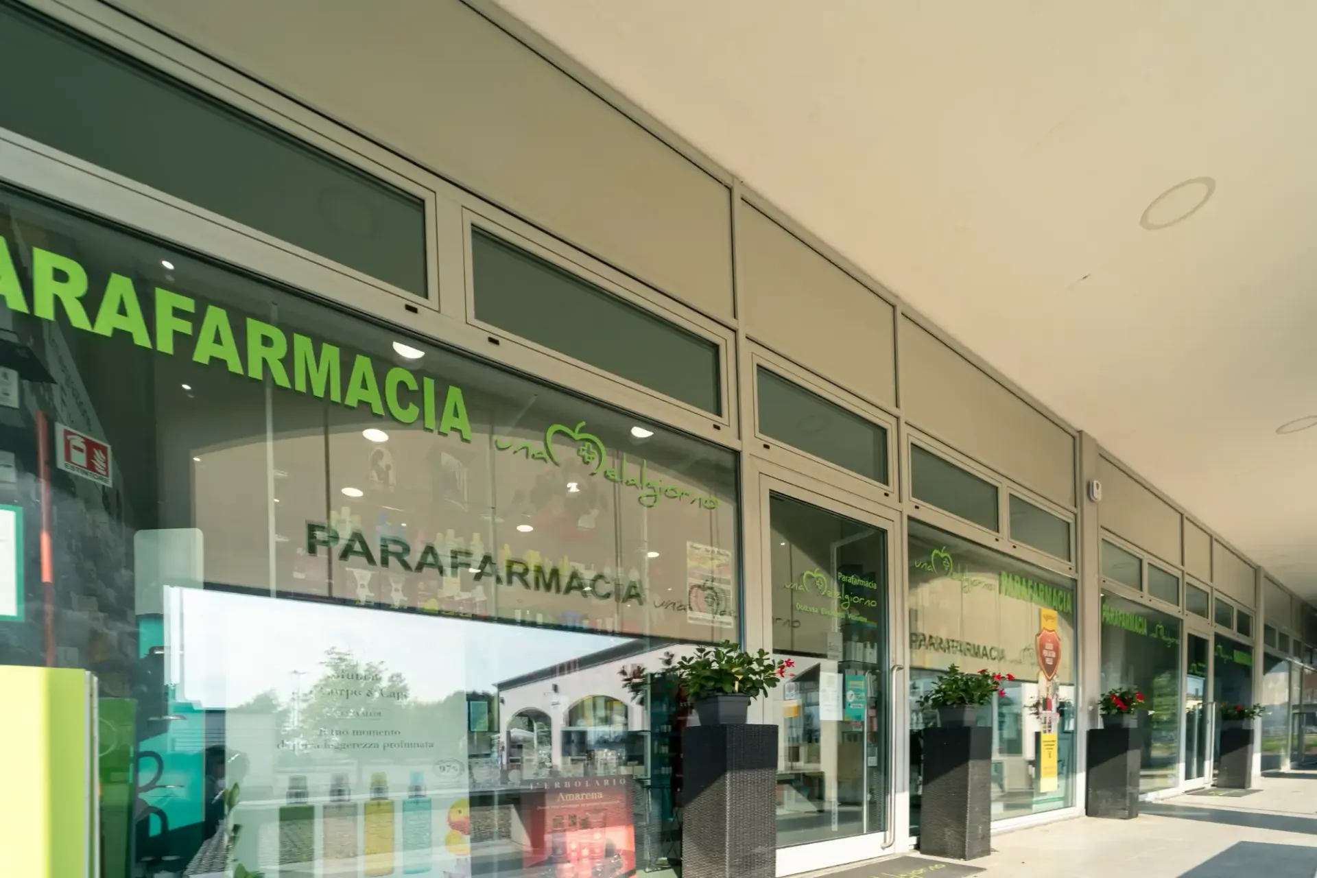 Facciata verde di una farmacia Parafarmacia con vetrine e passaggio esterno.