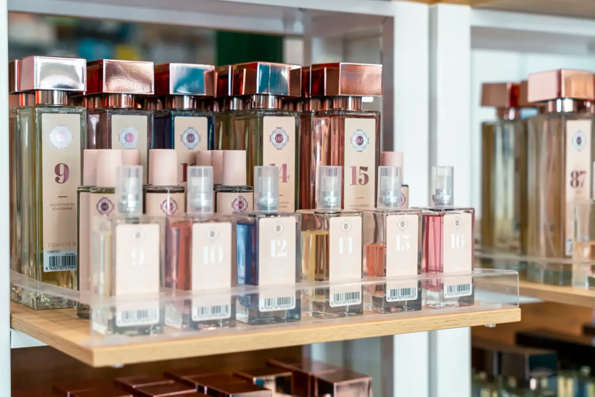 Flaconi di profumo esposti su scaffali di vetro in un negozio, con tappi color oro rosa e confezioni rosa tenue.