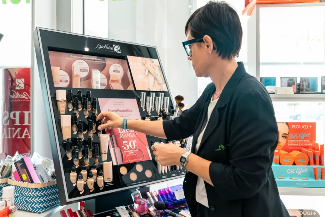 Una persona prova il trucco davanti a un espositore di cosmetici in un negozio luminoso.