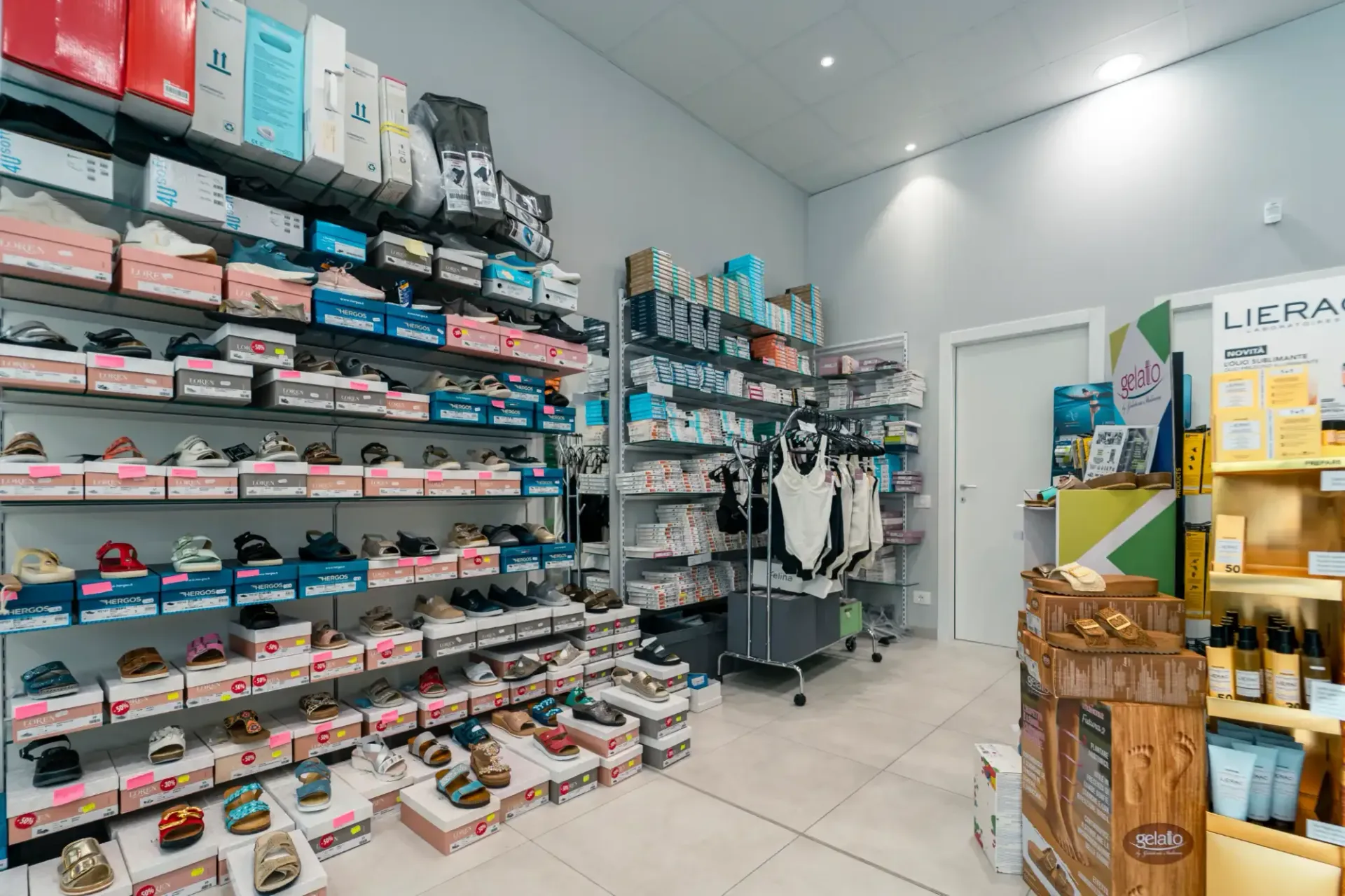 Luminoso interno di un negozio di scarpe con scaffali pieni di scarpe, scatole e appendiabiti.