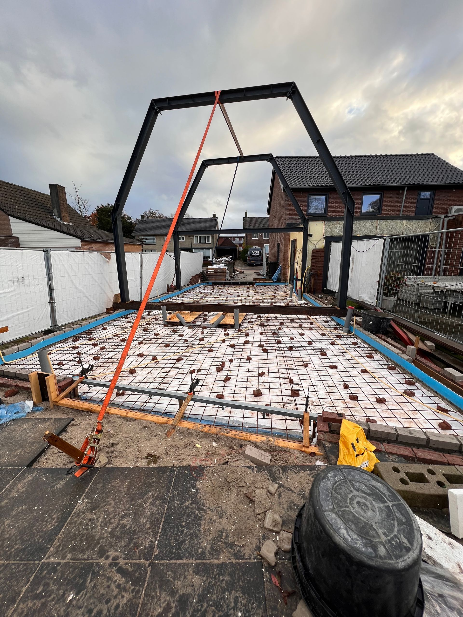 een zwarte emmer staat op de grond voor een gebouw in aanbouw