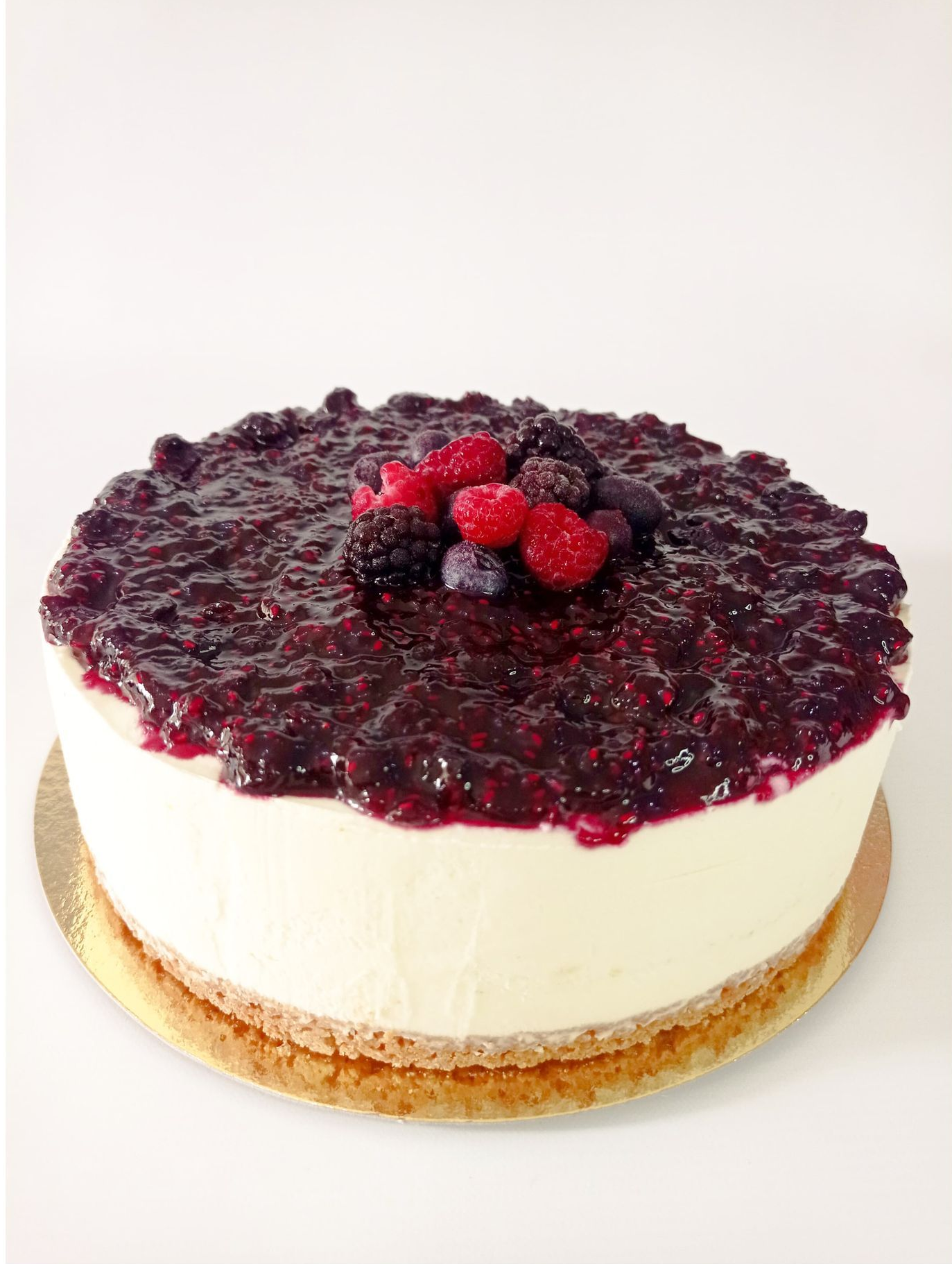 Tarta de queso redonda cubierta con compota de frutos rojos brillante y frambuesas frescas sobre un fondo blanco.