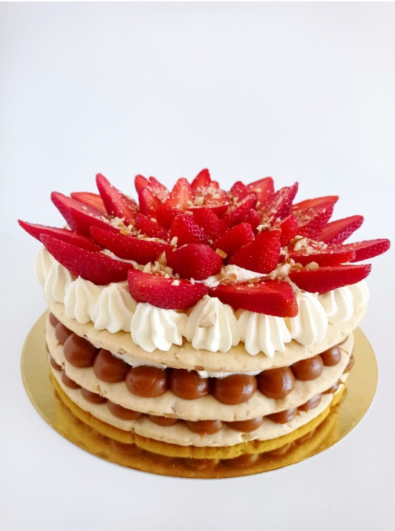Tarta de fresas en capas con crema batida y fresas frescas en rodajas sobre un fondo blanco.