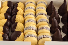 Surtido de pasteles cubiertos de chocolate y de chocolate amarillo, dispuestos en filas en una caja blanca.