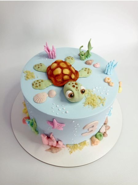 Tarta azul claro decorada con tortugas marinas y conchas sobre una base blanca para tartas.