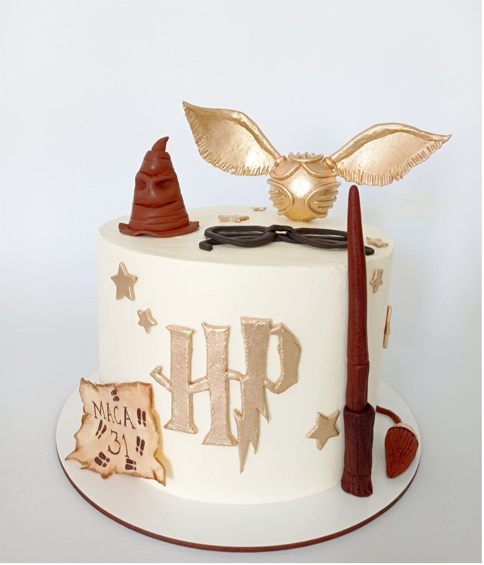 Tarta de cumpleaños blanca de Harry Potter con alas doradas, estrellas, varita, gafas, Sombrero Seleccionador e iniciales HP.