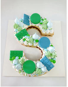 Galleta decorada con la letra S, con glaseado verde, azul y blanco sobre un fondo blanco.