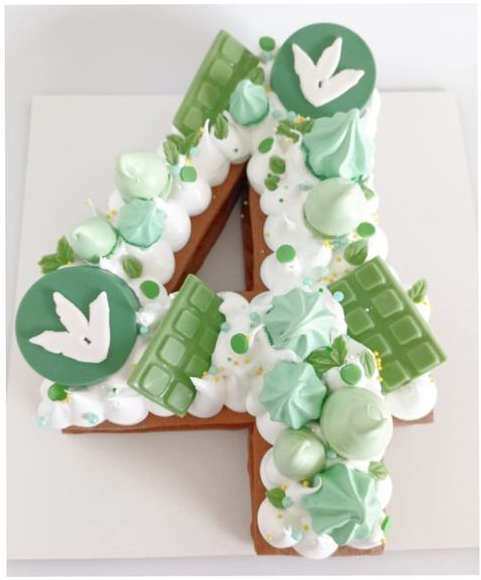 Tarta con el número 4 decorada en verde y blanco con adornos de conejitos sobre una superficie blanca.