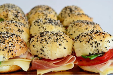 Mini sándwiches con panecillos de sésamo y amapola, rellenos de queso, jamón, tomate y lechuga.