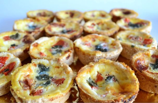 Mini quiches horneadas con queso fundido, espinacas y pimiento rojo, dispuestas en una bandeja.
