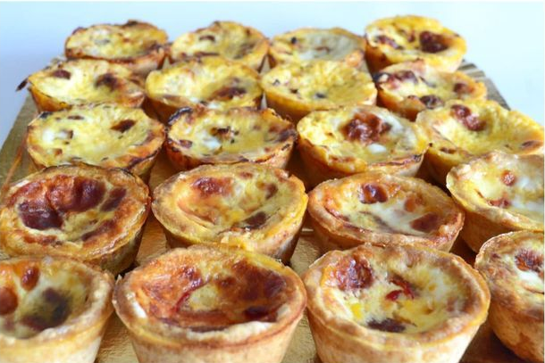 Bandeja de mini quiches surtidas con corteza dorada y rellenos cremosos.