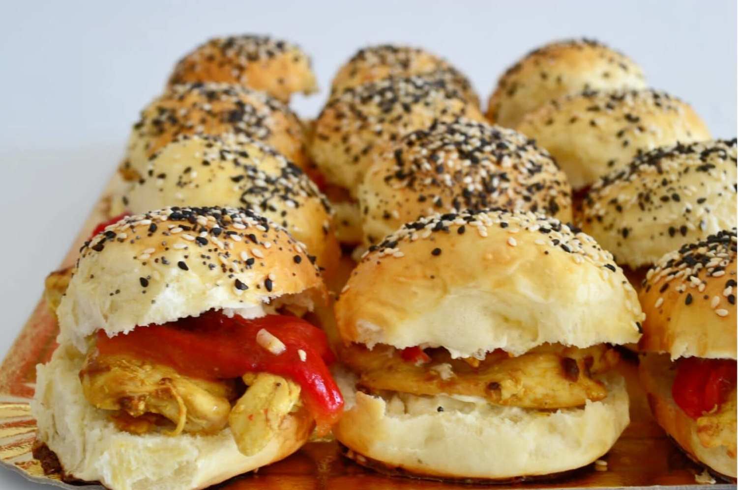 Bandeja de mini panecillos para sándwich con sésamo, pimiento rojo y relleno.
