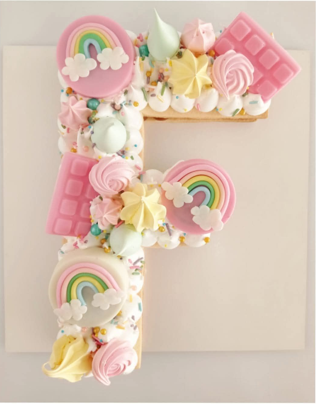 Letra F decorada con caramelos en tonos pastel, arcoíris, flores y detalles con estampado de gofre rosa.