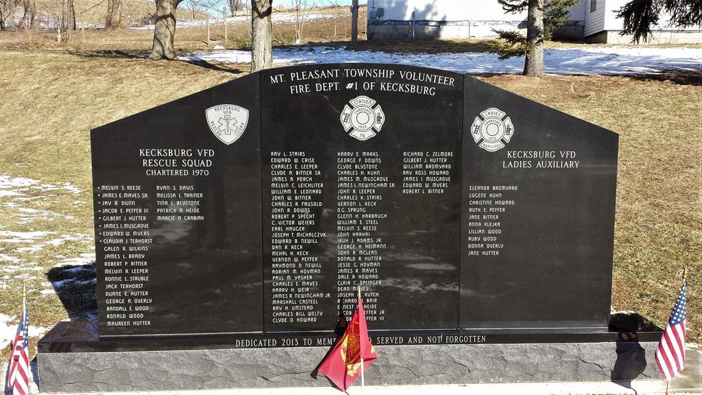 Black granite military memorial with engraved names and small American flags in a park setting