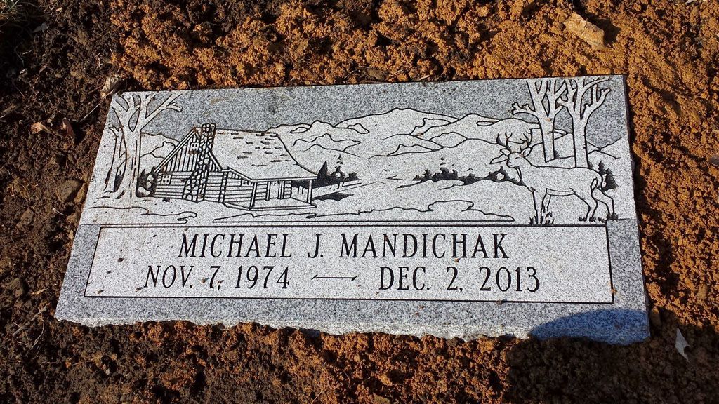 Engraved memorial plaque in dirt, reading “Michael J. Mandiczak, Aug. 4, 1974 – Dec. 2, 2015.”
