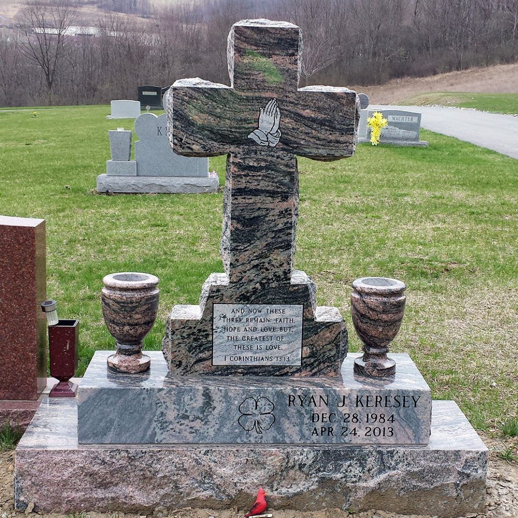 Weathered stone cross gravestone with urns in a cemetery on a grassy hillside