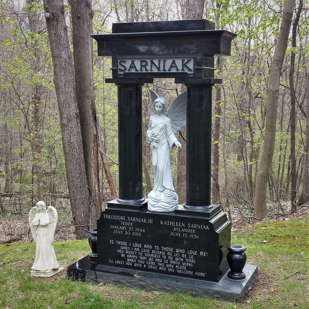 Black granite memorial with white statue and “SARNIAK” name in a wooded cemetery.