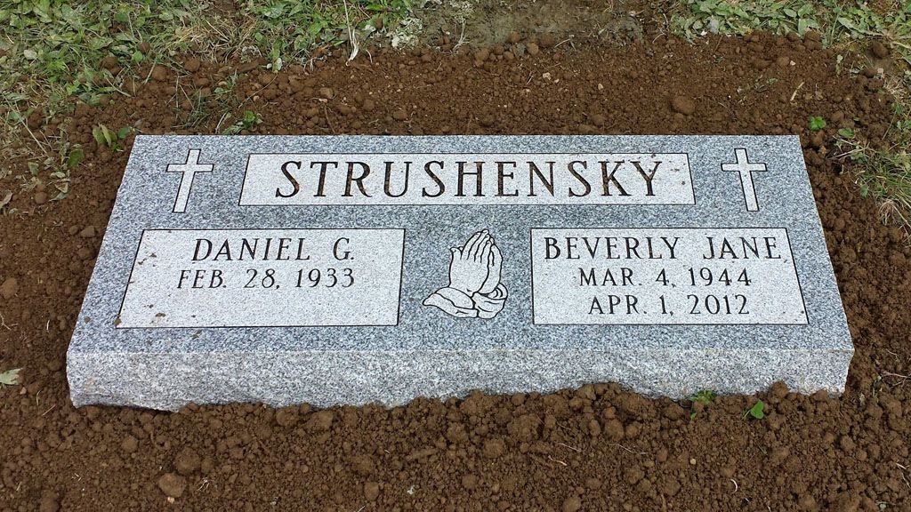 Gray granite gravestone engraved “STRUSHENSKY” with two name panels, set in mulch outdoors