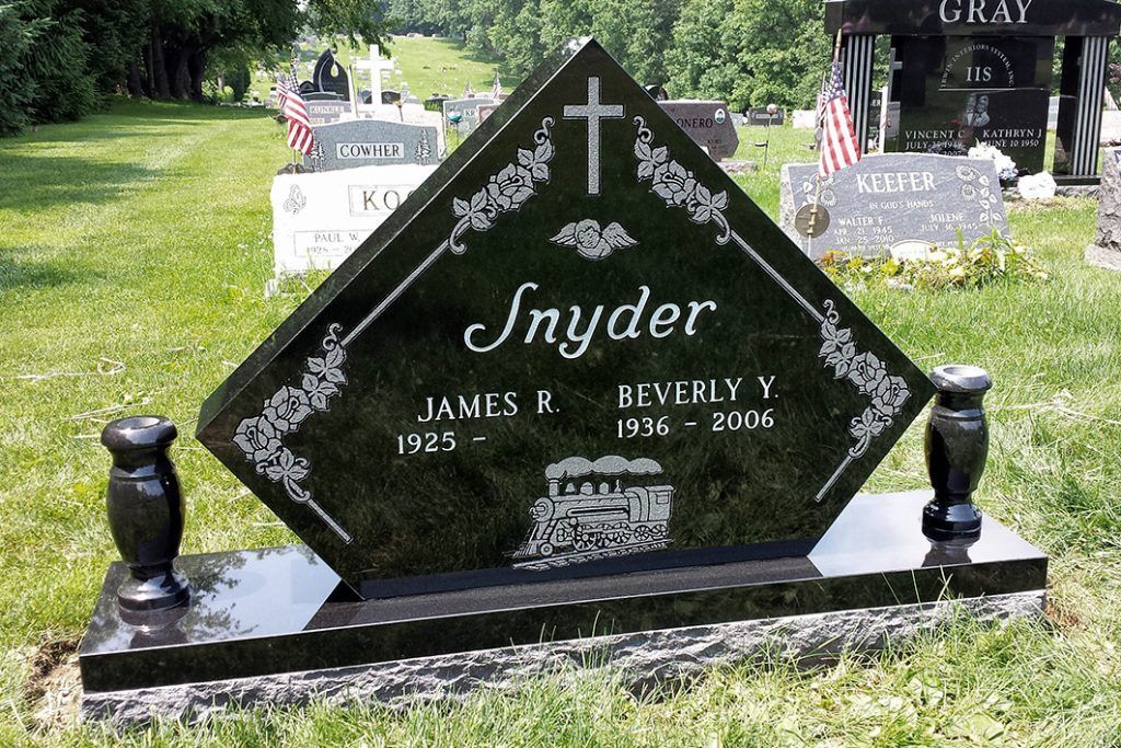 Black granite Snyder grave marker with white lettering in a grassy cemetery, flanked by small lamp posts.