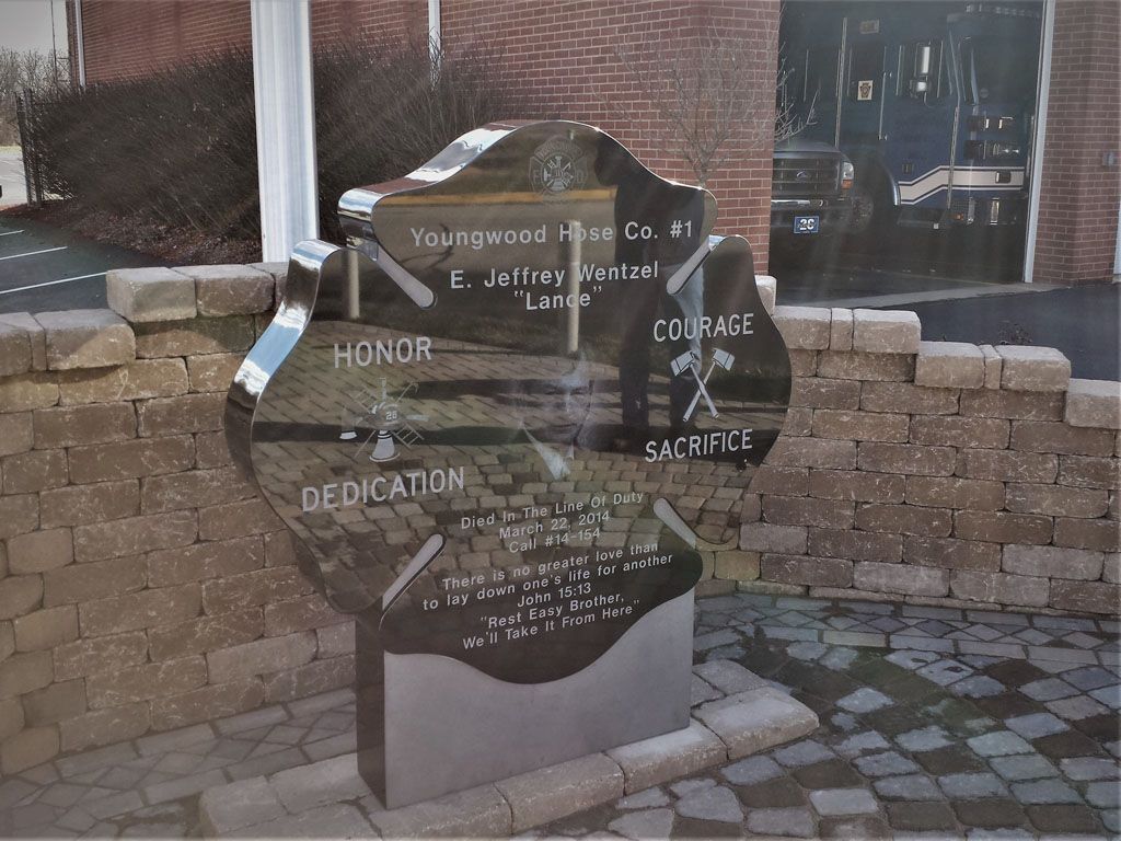 Black memorial sculpture with engraved words in a brick courtyard near a building entrance