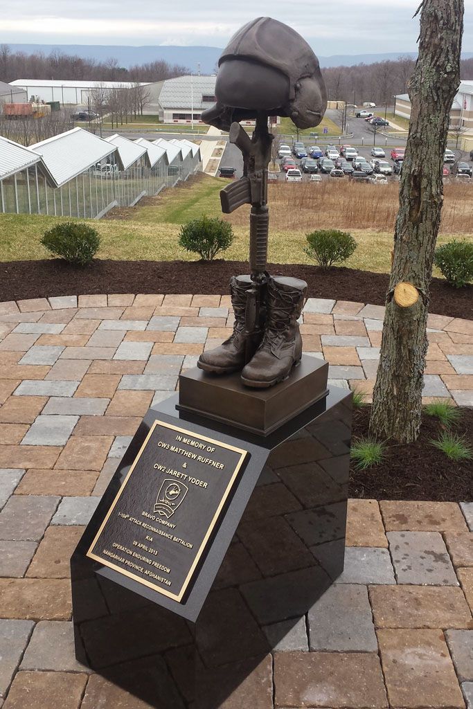 Bronze sculptural monument on a plaque-topped pedestal in a paved memorial garden overlooking a landscape