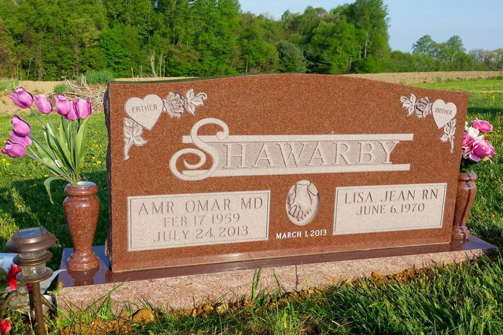 Brown memorial sign in a flower bed with pink flowers and bronze vases, reading “Shamrock.”