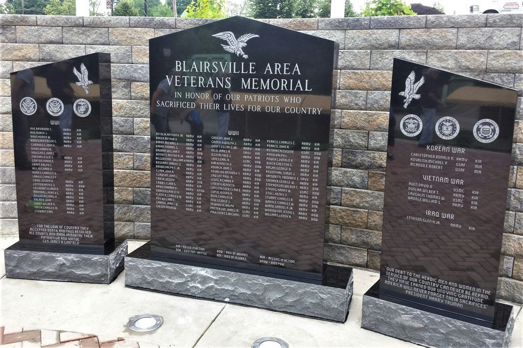 Three polished granite memorials with engraved names and symbols in an outdoor cemetery garden