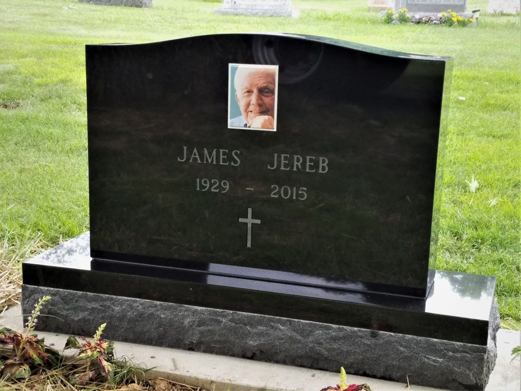 Black granite gravestone with a photo and the name James Jereb, set in a grassy cemetery.