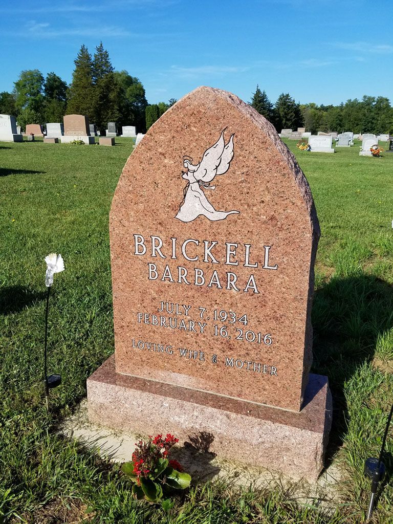 Pink granite gravestone with dove engraving in a cemetery, surrounded by green grass and flowers.